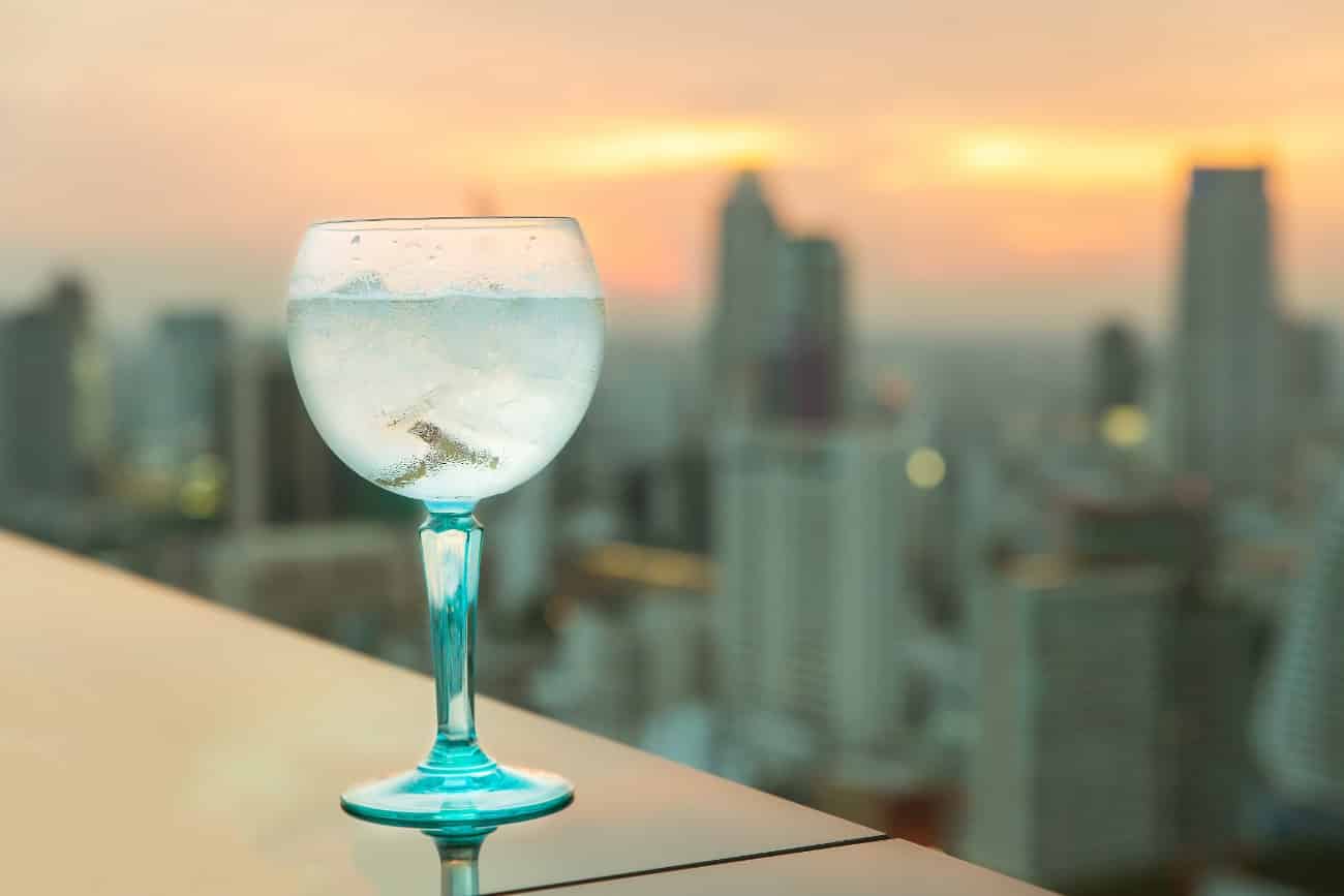 blue wine glass in focus in foreground on edge of rooftop with blurry skyline in background