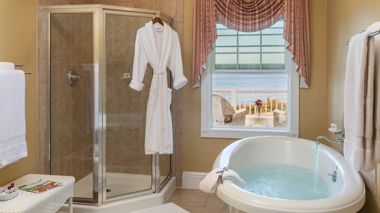 corner glass enclosed tiled shower, oval tubs being filled with view of private porch facing the ocean